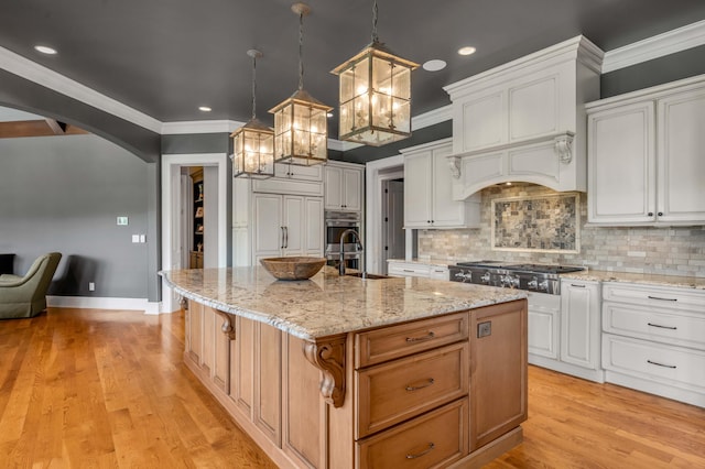 kitchen with arched walkways, pendant lighting, white cabinets, and an island with sink