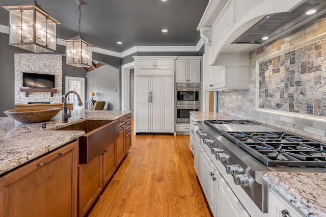 kitchen featuring pendant lighting, stainless steel appliances, brown cabinetry, white cabinets, and light stone countertops