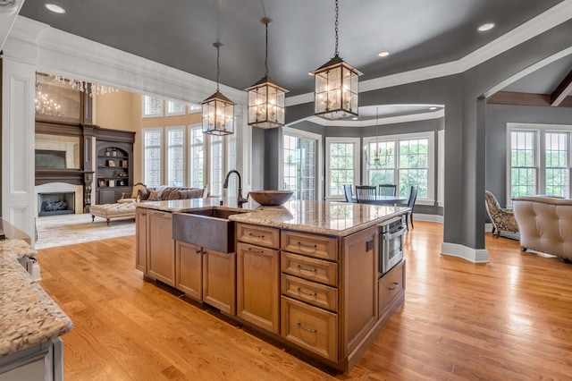 kitchen featuring brown cabinetry, open floor plan, hanging light fixtures, a kitchen island with sink, and a sink