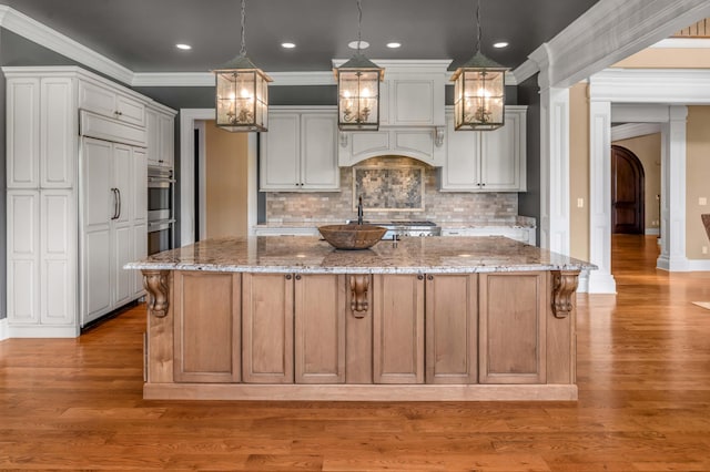 kitchen featuring wood finished floors, pendant lighting, a large island with sink, and light stone countertops