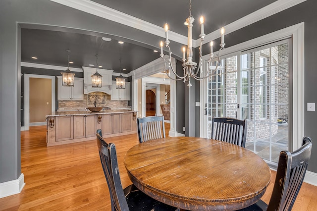 dining area featuring arched walkways, a notable chandelier, light wood-style floors, baseboards, and crown molding