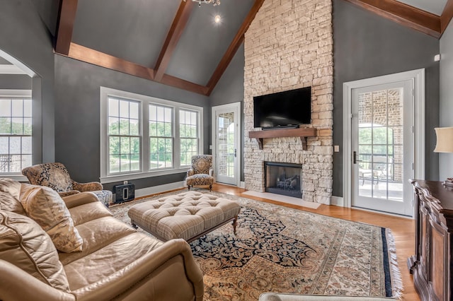 living room featuring baseboards, beamed ceiling, a stone fireplace, light wood-style floors, and high vaulted ceiling