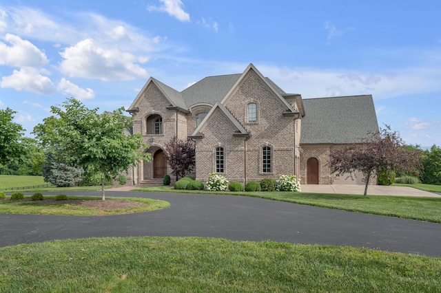 french country inspired facade featuring aphalt driveway, a front lawn, and brick siding