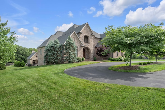 french country home with brick siding, a front lawn, and curved driveway