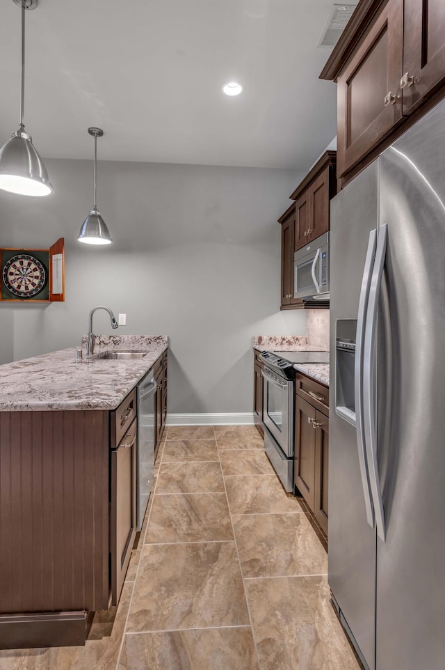 kitchen with dark brown cabinetry, light stone countertops, stainless steel appliances, pendant lighting, and a sink