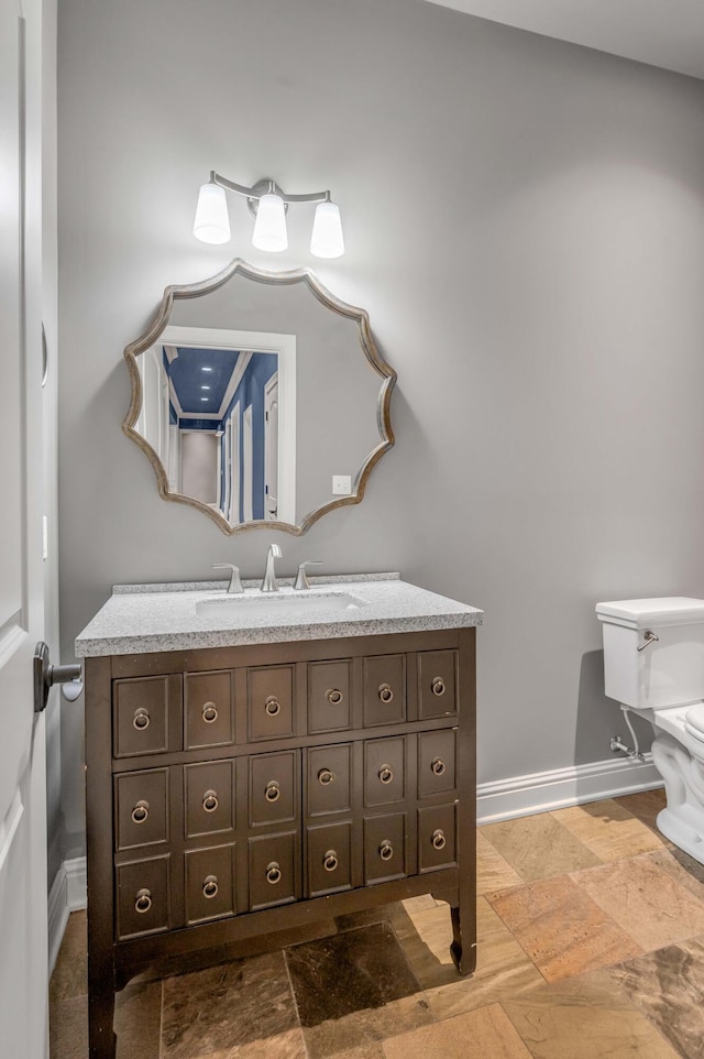 bathroom with toilet, stone finish flooring, baseboards, and vanity