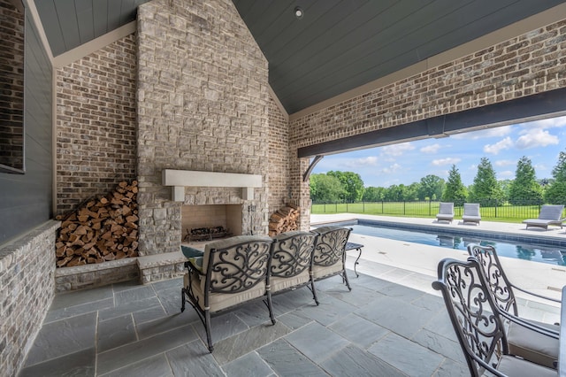 view of patio featuring an outdoor stone fireplace, fence, and a fenced in pool