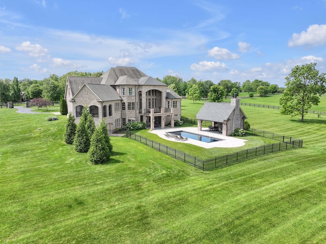 rear view of property featuring a balcony, a fenced backyard, a lawn, and a rural view