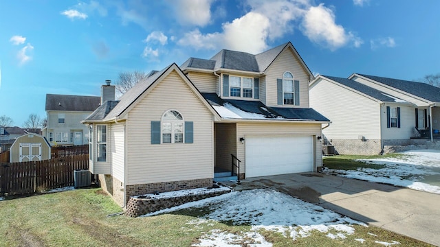 traditional-style home with central AC unit, an attached garage, a shingled roof, fence, and concrete driveway