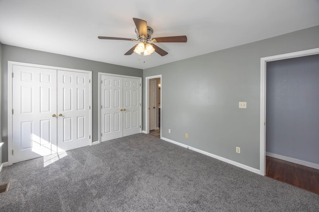 unfurnished bedroom featuring a ceiling fan, dark colored carpet, baseboards, and two closets