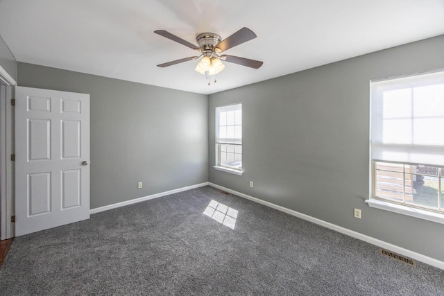 empty room featuring ceiling fan, visible vents, baseboards, and dark carpet