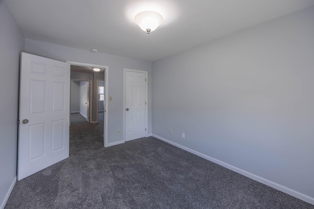 unfurnished bedroom with dark carpet and baseboards