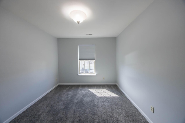 spare room with dark colored carpet, visible vents, and baseboards