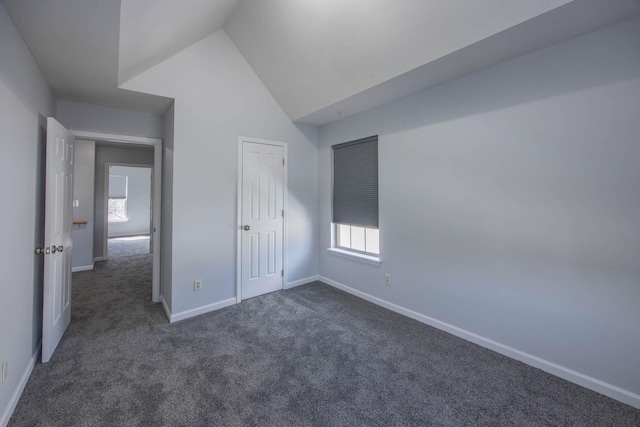 unfurnished bedroom with lofted ceiling, baseboards, and dark carpet