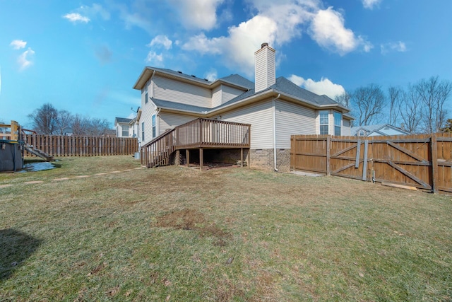 back of house featuring fence, a yard, a wooden deck, a gate, and a chimney