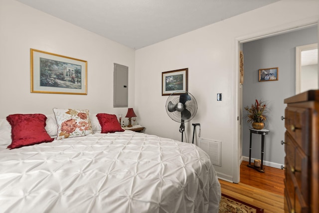 bedroom with electric panel, visible vents, baseboards, and wood finished floors