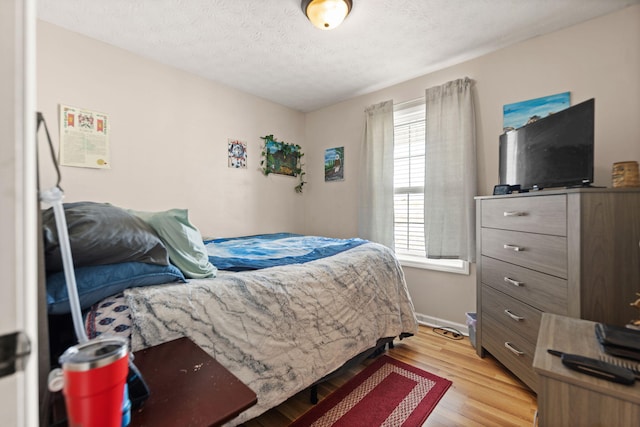 bedroom featuring a textured ceiling, light wood-style flooring, and baseboards