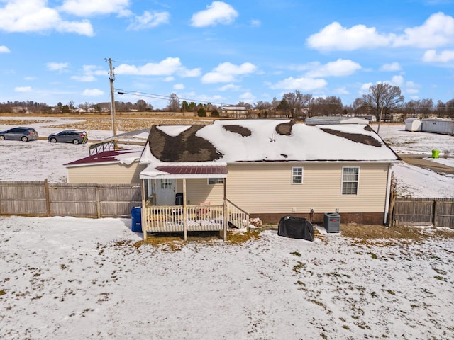 snow covered house featuring fence, central AC unit, and a wooden deck