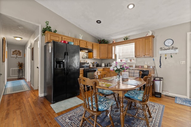 kitchen with under cabinet range hood, visible vents, baseboards, light wood-style floors, and black appliances