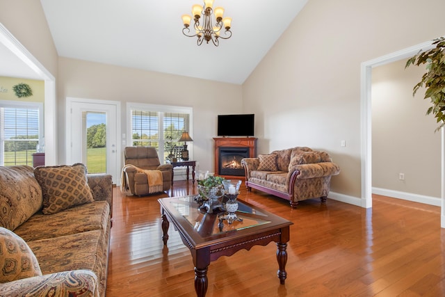 living area with high vaulted ceiling, wood finished floors, baseboards, a glass covered fireplace, and an inviting chandelier