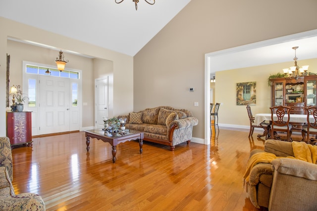 living room featuring a chandelier, high vaulted ceiling, baseboards, and wood finished floors