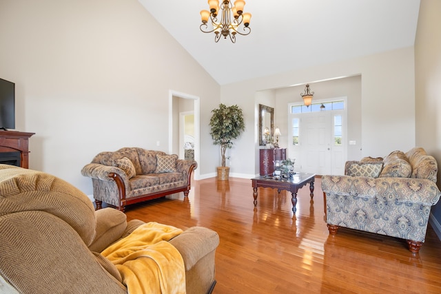 living room featuring high vaulted ceiling, a notable chandelier, a fireplace, wood finished floors, and baseboards