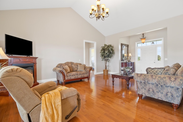 living area with high vaulted ceiling, a glass covered fireplace, wood finished floors, and baseboards