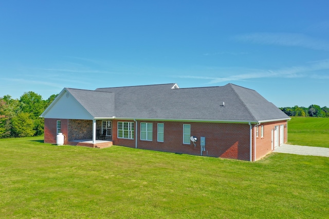 rear view of property with a garage, brick siding, a yard, and driveway