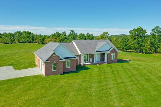 view of front of property featuring a front yard, covered porch, driveway, and a wooded view