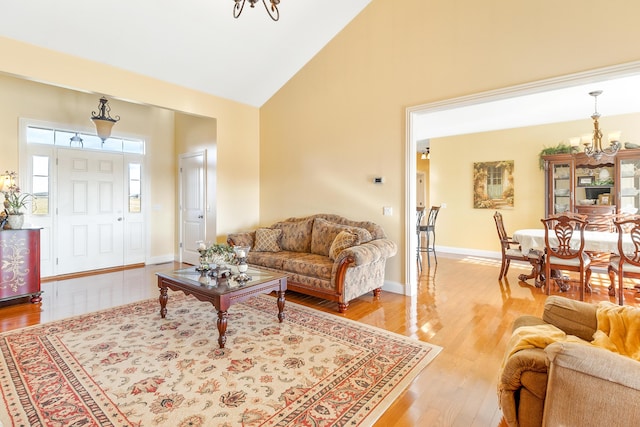 living room with high vaulted ceiling, baseboards, light wood finished floors, and an inviting chandelier