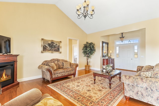 living area featuring baseboards, high vaulted ceiling, wood finished floors, and a glass covered fireplace