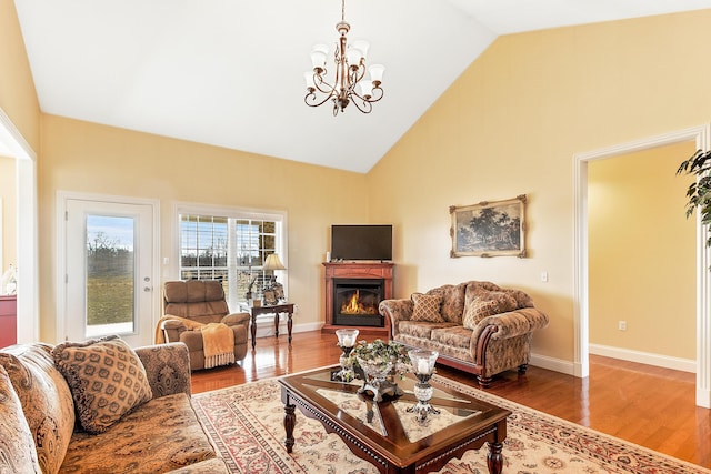 living room featuring high vaulted ceiling, a glass covered fireplace, baseboards, and wood finished floors