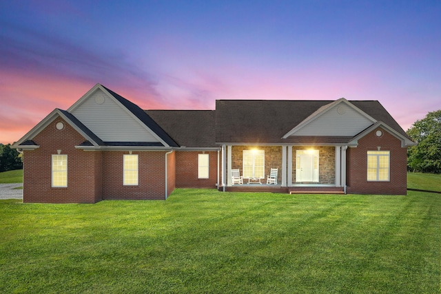 back of house at dusk with a porch, a lawn, and brick siding