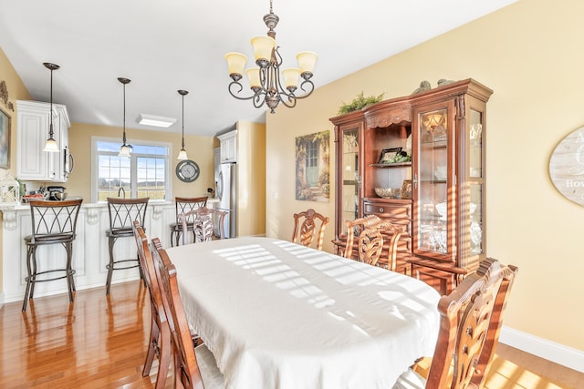 dining space featuring baseboards, light wood-type flooring, and an inviting chandelier