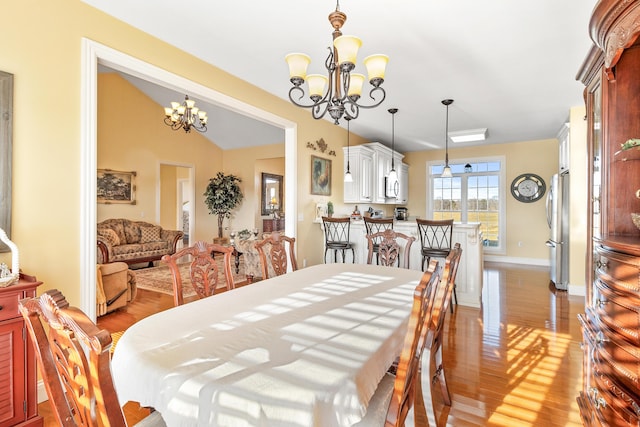 dining area with lofted ceiling, light wood-style floors, baseboards, and an inviting chandelier