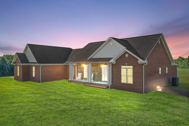 back of house at dusk with brick siding, central AC unit, and a yard