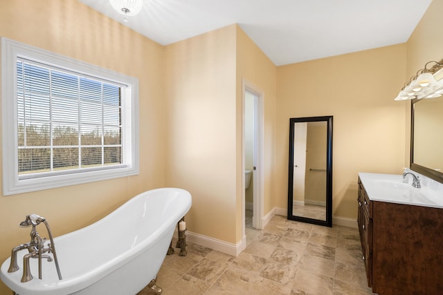 bathroom with toilet, baseboards, a freestanding bath, and vanity