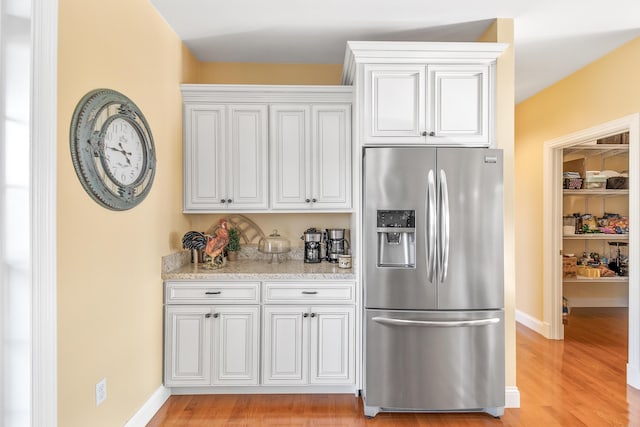 kitchen with light stone countertops, stainless steel fridge, white cabinets, and light wood finished floors