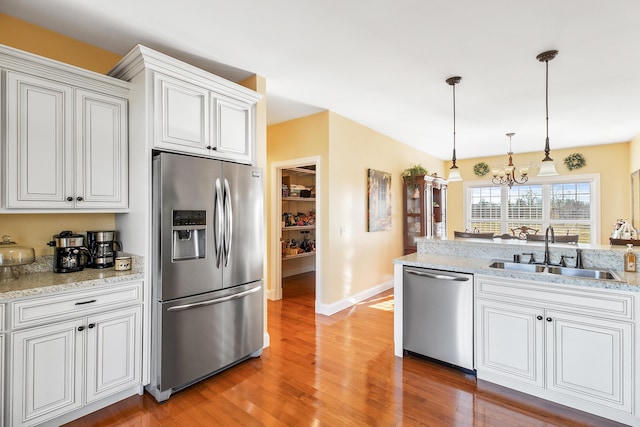 kitchen with decorative light fixtures, appliances with stainless steel finishes, white cabinetry, a sink, and wood finished floors