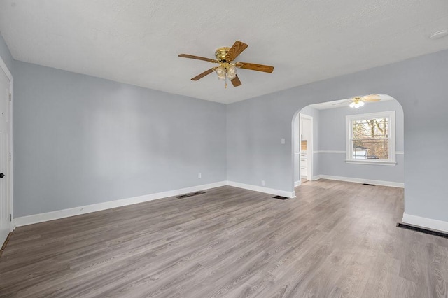 spare room featuring arched walkways, light wood-style flooring, visible vents, and baseboards