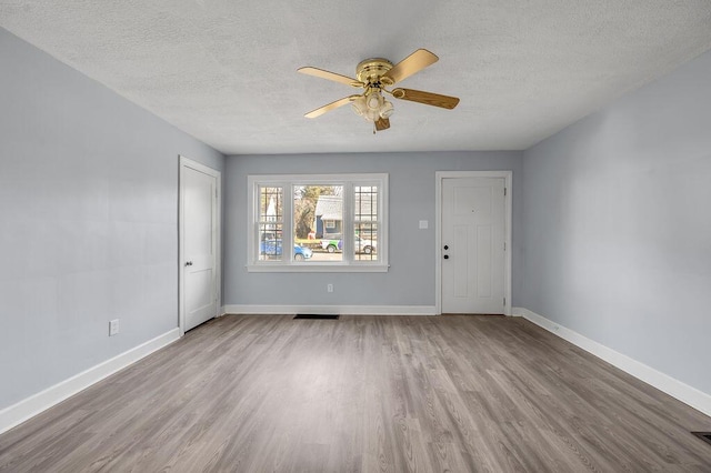 empty room featuring a textured ceiling, light wood-style flooring, and baseboards