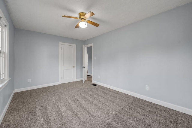 unfurnished room with carpet, visible vents, baseboards, and ceiling fan