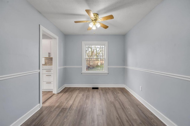 spare room with dark wood-style floors, a ceiling fan, and baseboards