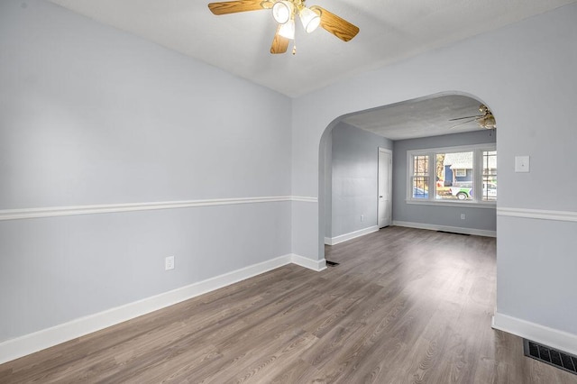 empty room with arched walkways, ceiling fan, baseboards, and wood finished floors