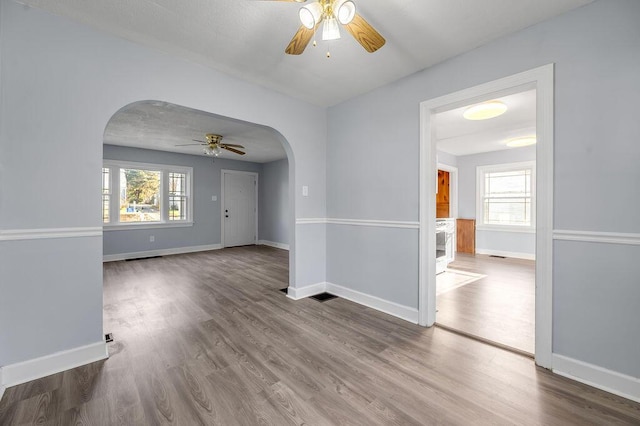 spare room with baseboards, arched walkways, a ceiling fan, and wood finished floors