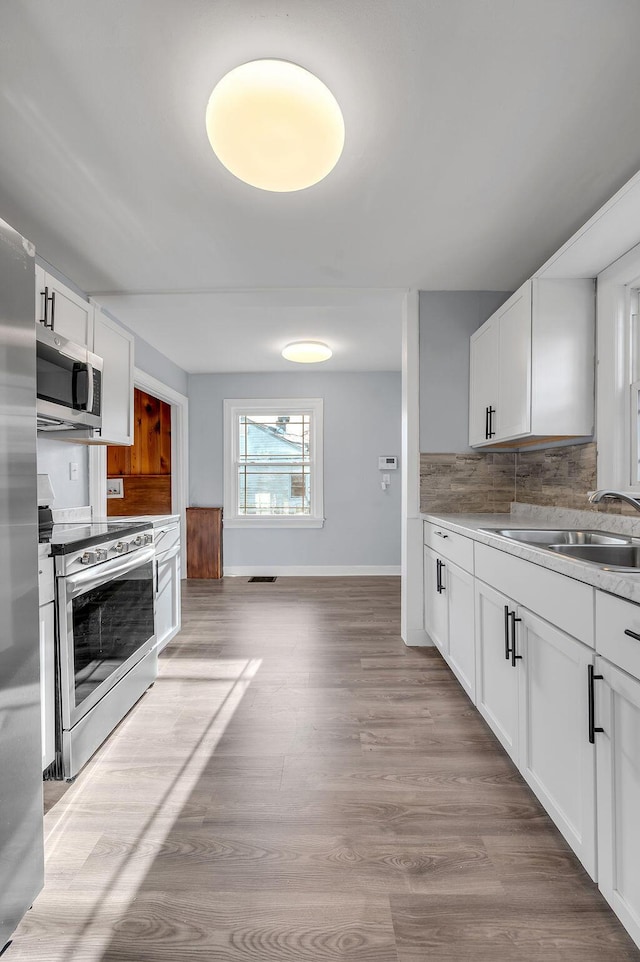 kitchen with tasteful backsplash, light countertops, appliances with stainless steel finishes, white cabinets, and a sink