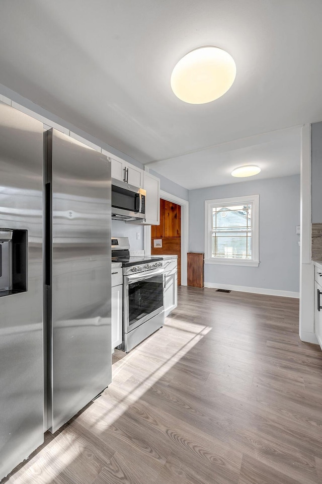 kitchen featuring appliances with stainless steel finishes, light countertops, light wood-style floors, and white cabinetry