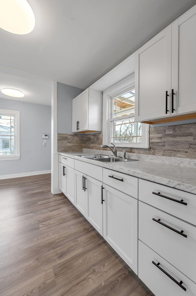 kitchen featuring tasteful backsplash, baseboards, white cabinets, light wood-style floors, and a sink