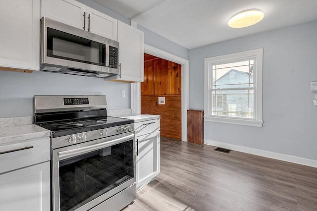 kitchen featuring stainless steel appliances, visible vents, baseboards, white cabinets, and light wood finished floors