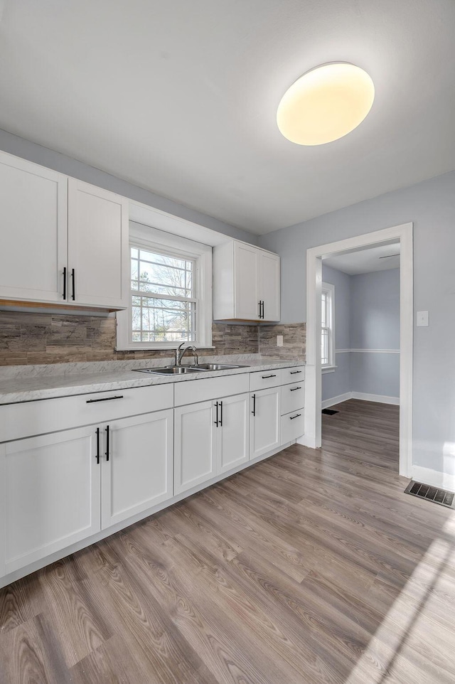 kitchen with tasteful backsplash, visible vents, light wood-style flooring, white cabinetry, and baseboards